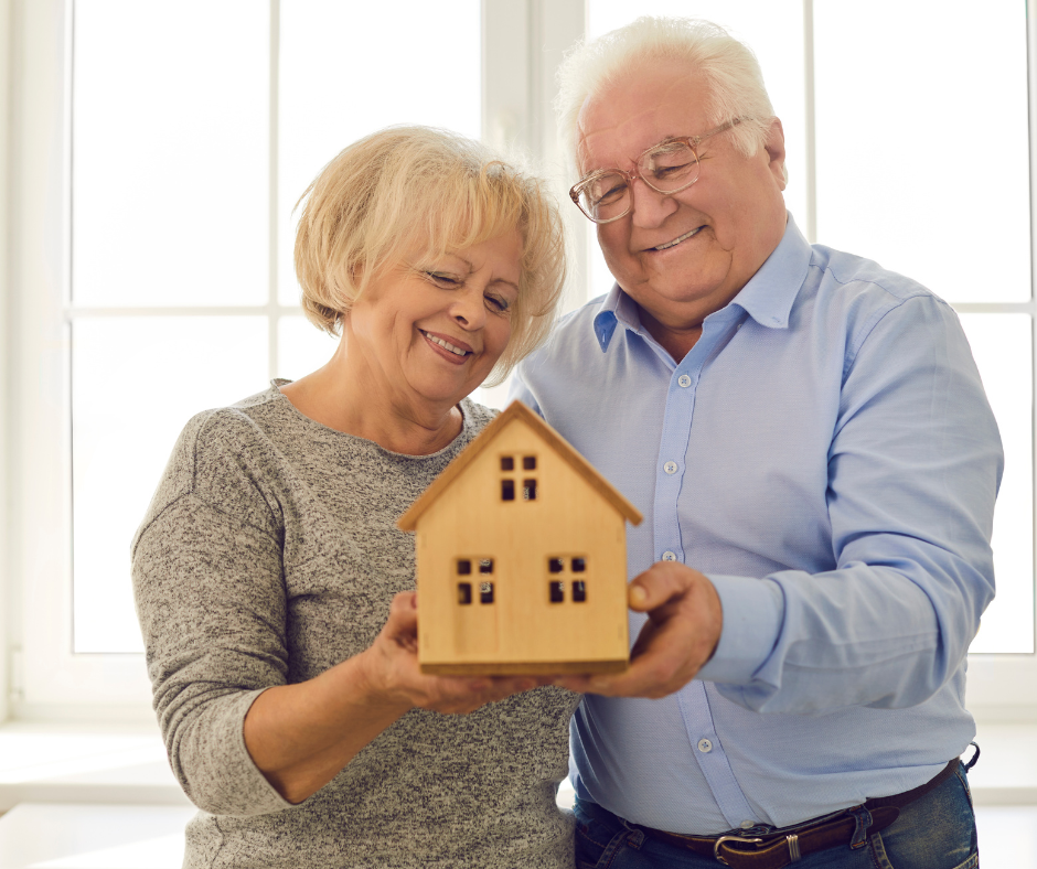 Older couple holding a model house and smiling.